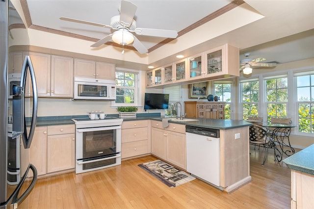 kitchen featuring light wood finished floors, light brown cabinets, a sink, white appliances, and a peninsula