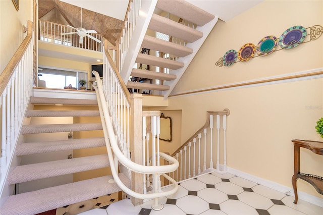 stairway featuring a ceiling fan, a towering ceiling, baseboards, and tile patterned floors