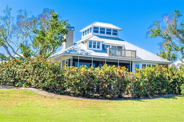 rear view of house with a yard, a chimney, a sunroom, metal roof, and a balcony