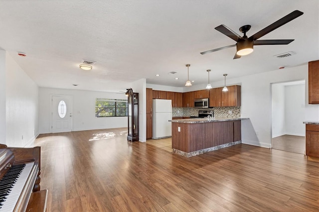 kitchen featuring brown cabinets, a peninsula, decorative backsplash, appliances with stainless steel finishes, and open floor plan