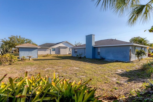 back of property featuring stucco siding, a yard, and a chimney