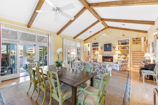 dining room with light wood-type flooring, beam ceiling, a fireplace, and stairway