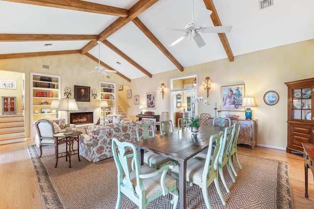 dining space with light wood-style flooring, a fireplace, visible vents, stairway, and beam ceiling