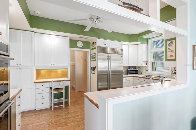 kitchen featuring tasteful backsplash, appliances with stainless steel finishes, light countertops, white cabinetry, and a sink