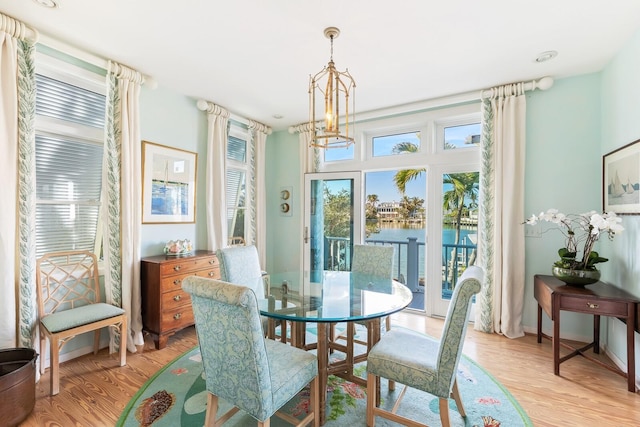 dining area featuring a chandelier, a water view, light wood-style flooring, and baseboards