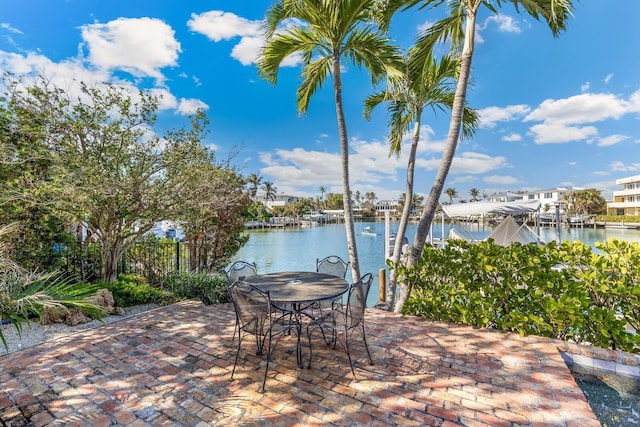 view of patio with outdoor dining area, a water view, fence, and a boat dock