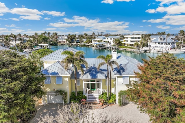 exterior space featuring driveway, a garage, a residential view, metal roof, and a water view