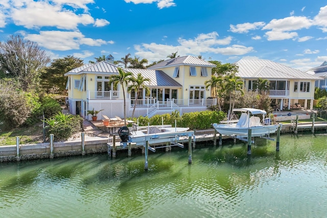 rear view of house with a water view, a standing seam roof, boat lift, and metal roof