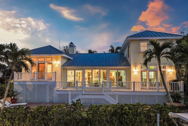 back of property at dusk featuring a chimney, stairway, metal roof, a standing seam roof, and a porch