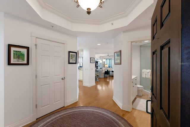 entrance foyer with light wood-type flooring, baseboards, a raised ceiling, and crown molding