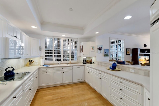 kitchen with a tray ceiling, white appliances, crown molding, and a sink