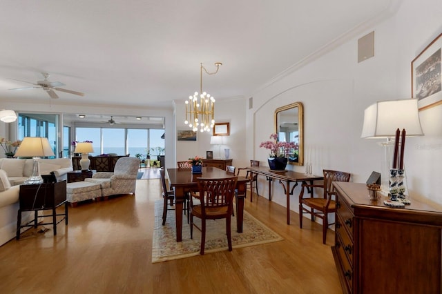 dining space featuring crown molding, light wood-style flooring, and ceiling fan with notable chandelier