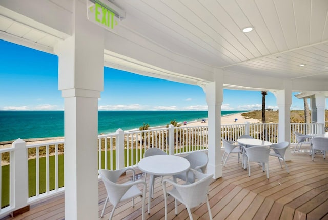 wooden deck with outdoor dining space, a beach view, and a water view