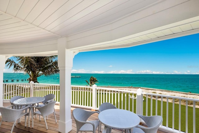 wooden terrace with a water view, outdoor dining area, a view of the beach, and a yard