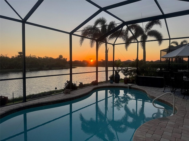 pool at dusk with a lanai, a patio area, a water view, and an outdoor pool