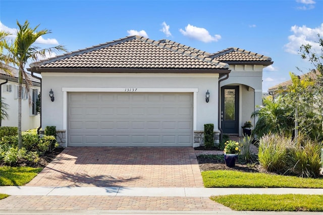 mediterranean / spanish-style home featuring a garage, stone siding, a tile roof, decorative driveway, and stucco siding