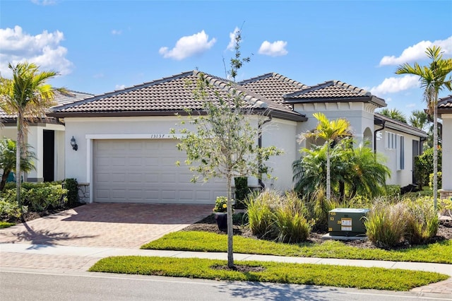 13137 Oriago St, Venice, FL 34293 - mediterranean / spanish home featuring a tile roof, decorative driveway, stone siding, a garage, and stucco siding
