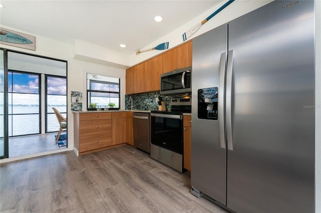 kitchen with recessed lighting, stainless steel appliances, wood finished floors, brown cabinets, and tasteful backsplash