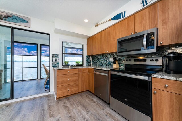 kitchen with light stone counters, appliances with stainless steel finishes, brown cabinets, light wood finished floors, and tasteful backsplash