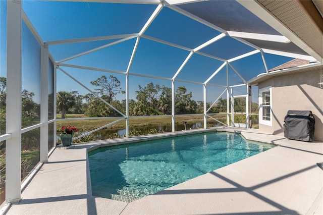 outdoor pool with glass enclosure, a patio, area for grilling, and a water view