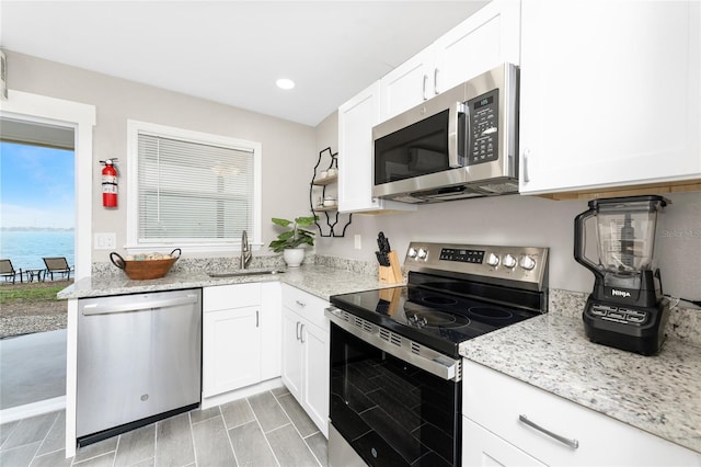 kitchen featuring white cabinets, light stone countertops, stainless steel appliances, and a sink