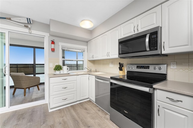 kitchen with light wood-style flooring, a sink, white cabinets, light countertops, and appliances with stainless steel finishes