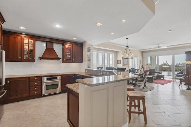 kitchen with a peninsula, premium range hood, a kitchen bar, stainless steel oven, and a sink