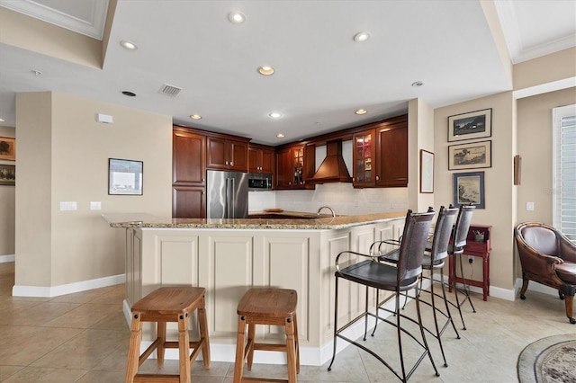 kitchen featuring custom exhaust hood, decorative backsplash, light stone countertops, a peninsula, and high end refrigerator