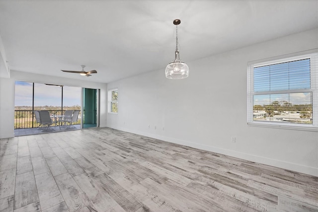 unfurnished room with ceiling fan with notable chandelier, light wood-style flooring, and baseboards