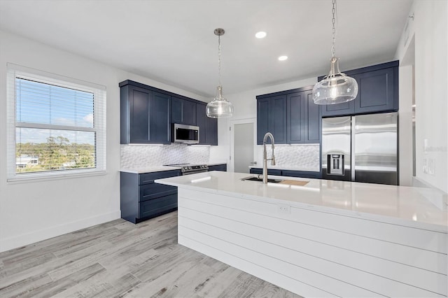 kitchen featuring light countertops, backsplash, appliances with stainless steel finishes, light wood-style floors, and a sink