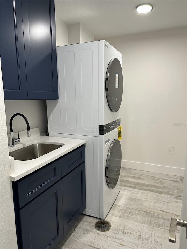 washroom with cabinet space, baseboards, light wood-style flooring, stacked washing maching and dryer, and a sink