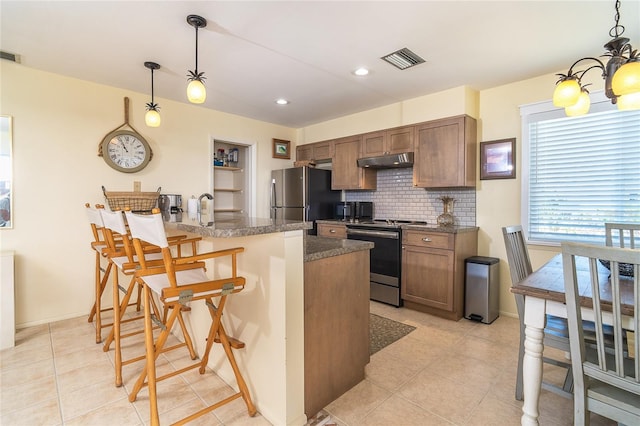 kitchen with under cabinet range hood, visible vents, appliances with stainless steel finishes, decorative backsplash, and a kitchen bar