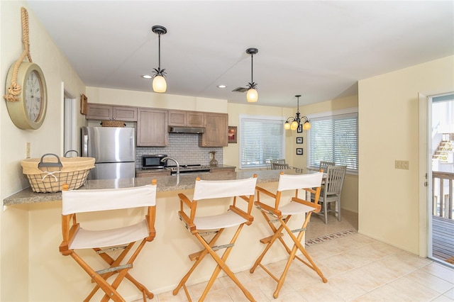 kitchen with decorative backsplash, a breakfast bar area, stainless steel appliances, under cabinet range hood, and pendant lighting