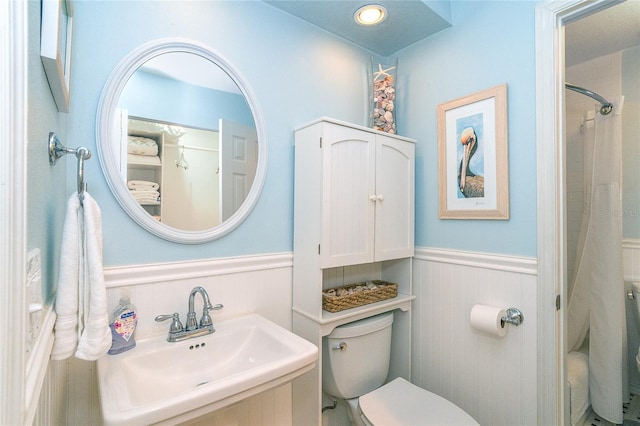 full bath featuring toilet, a sink, and wainscoting