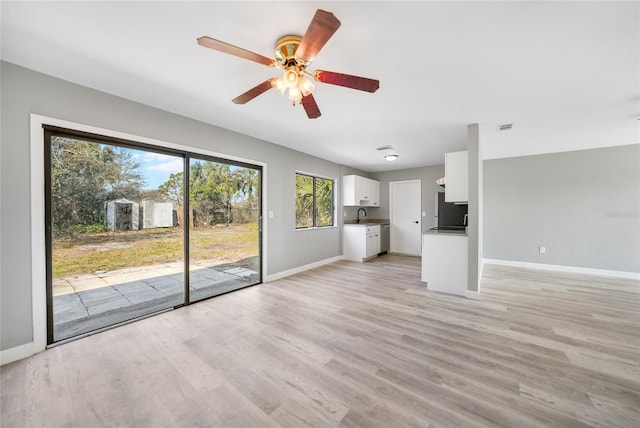 unfurnished living room featuring ceiling fan, a sink, visible vents, baseboards, and light wood-type flooring