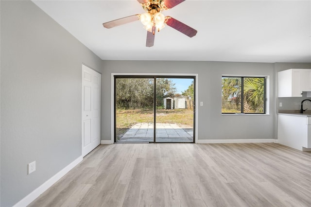 unfurnished living room featuring light wood-style floors, a sink, baseboards, and ceiling fan