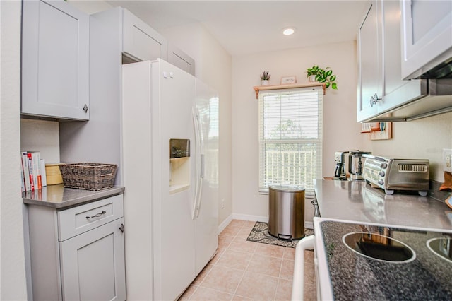 kitchen with white refrigerator with ice dispenser, a toaster, light tile patterned floors, dark countertops, and baseboards