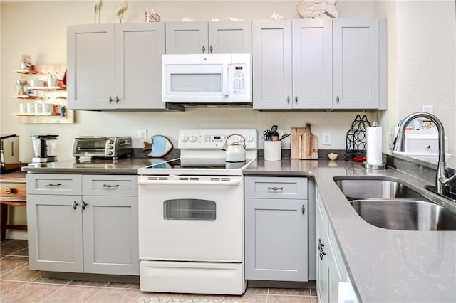 kitchen with light tile patterned flooring, a toaster, white appliances, a sink, and gray cabinets