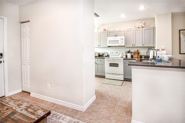 kitchen featuring light tile patterned floors, dark countertops, a sink, white appliances, and baseboards