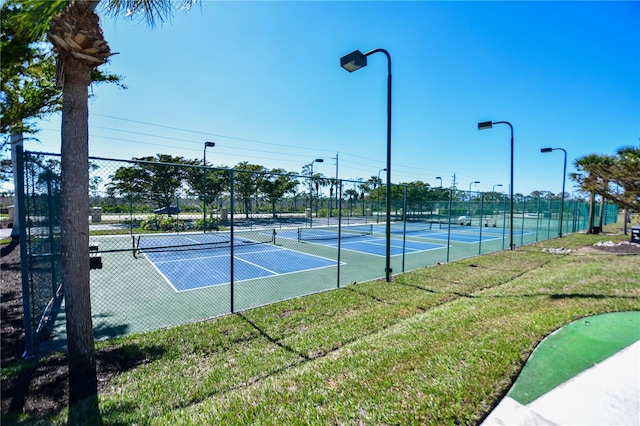 view of tennis court featuring a lawn and fence