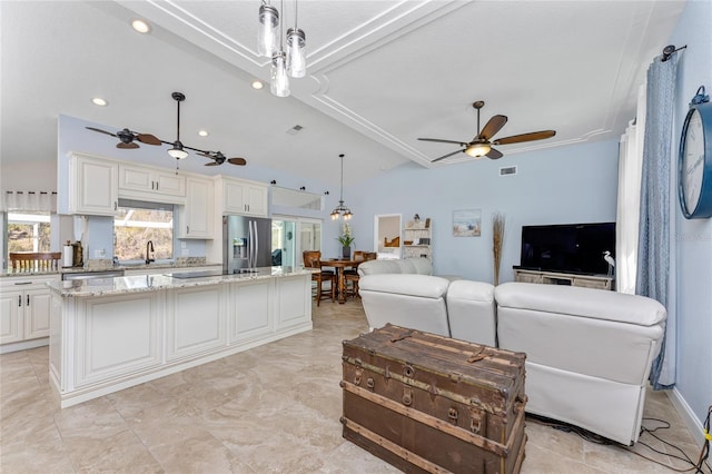 kitchen with a ceiling fan, stainless steel refrigerator with ice dispenser, a kitchen island, light stone countertops, and vaulted ceiling