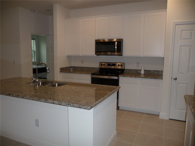 kitchen featuring appliances with stainless steel finishes, white cabinetry, a sink, light tile patterned flooring, and dark stone countertops