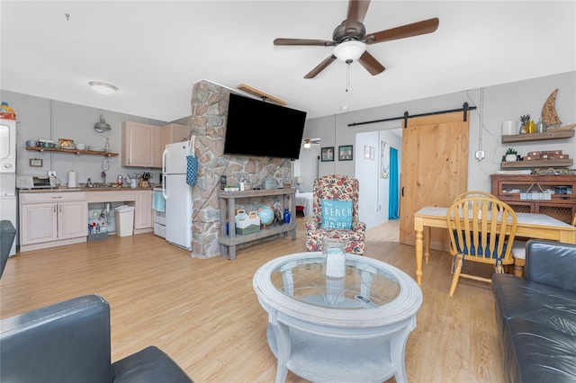 living area featuring stacked washer and dryer, a barn door, a ceiling fan, and light wood-style floors