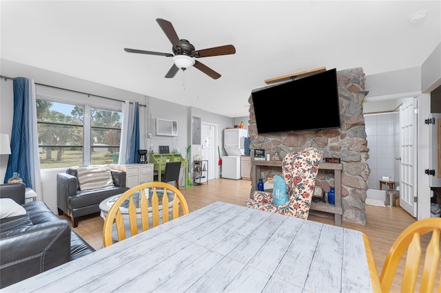 dining area featuring ceiling fan, a stone fireplace, a wall mounted AC, and wood finished floors