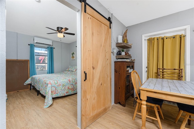 bedroom featuring light wood-style floors, a barn door, a ceiling fan, and a wall mounted air conditioner