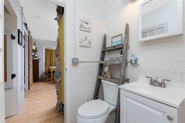 bathroom with toilet, tile walls, vanity, and wood finished floors