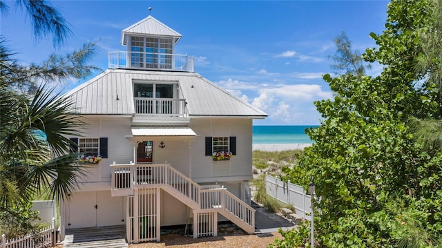 view of front of property featuring a water view, fence, stairway, metal roof, and a balcony