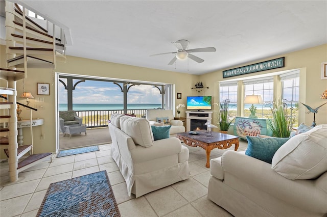 tiled living area featuring a warm lit fireplace and a ceiling fan