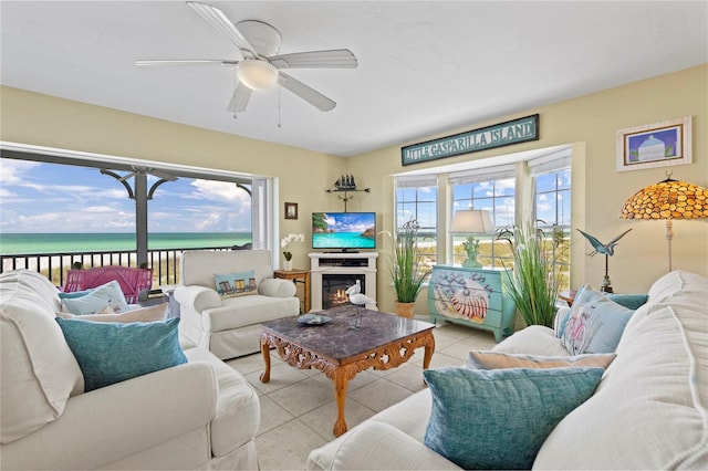 living area with a glass covered fireplace, light tile patterned flooring, a ceiling fan, and a water view