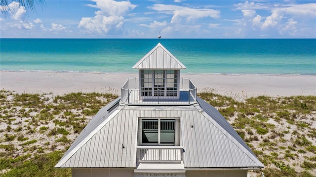 exterior space featuring board and batten siding, metal roof, a view of the beach, and a water view